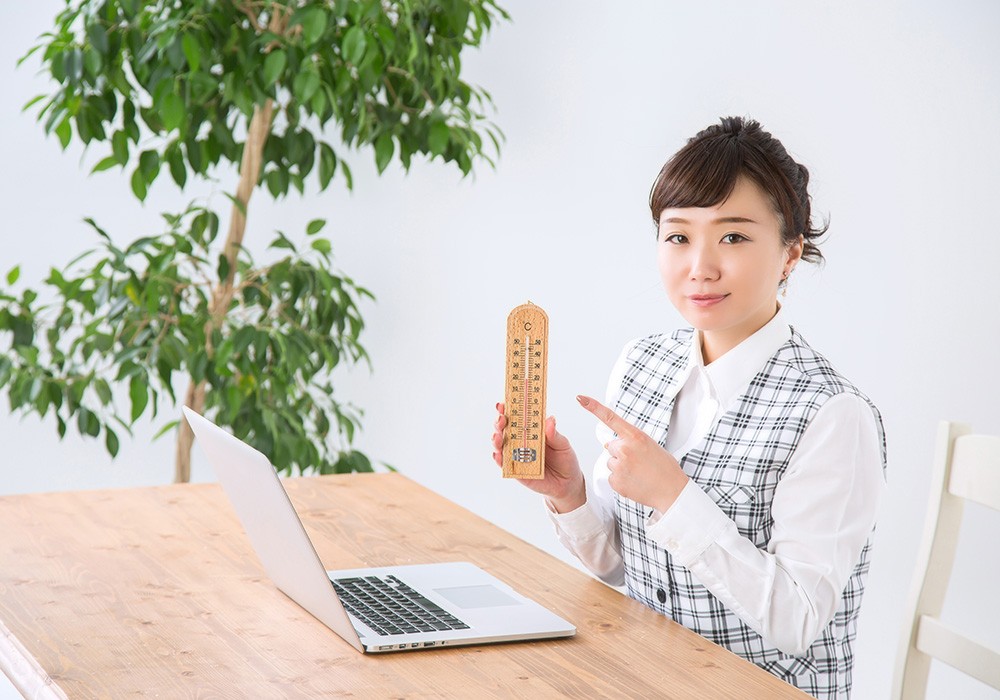 オフィスで温度計を持って冷房管理するビジネスウーマン