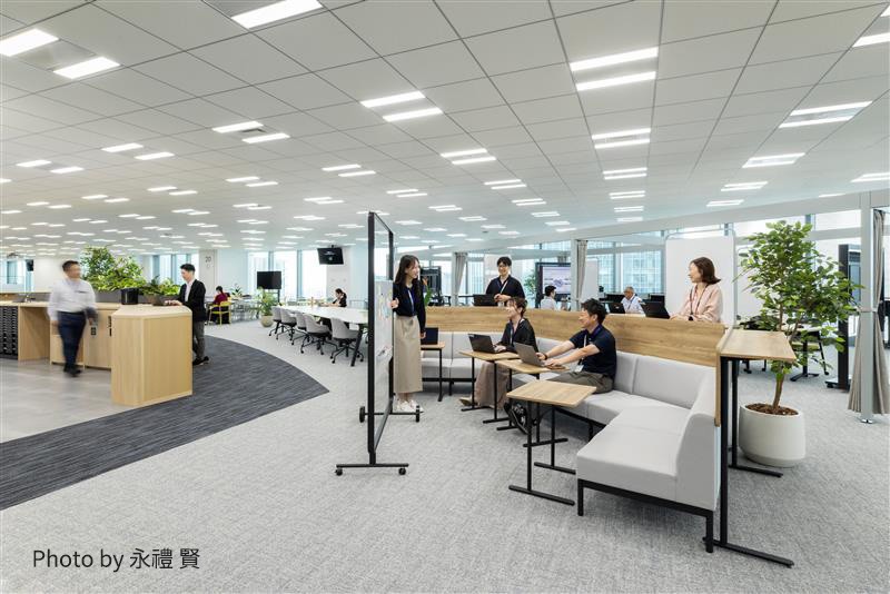 広いオフィススペースで、複数の社員が作業や会話をしている様子。快適な家具や緑の植物も配置された現代的なオフィス環境。（Photo by 永禮 賢）